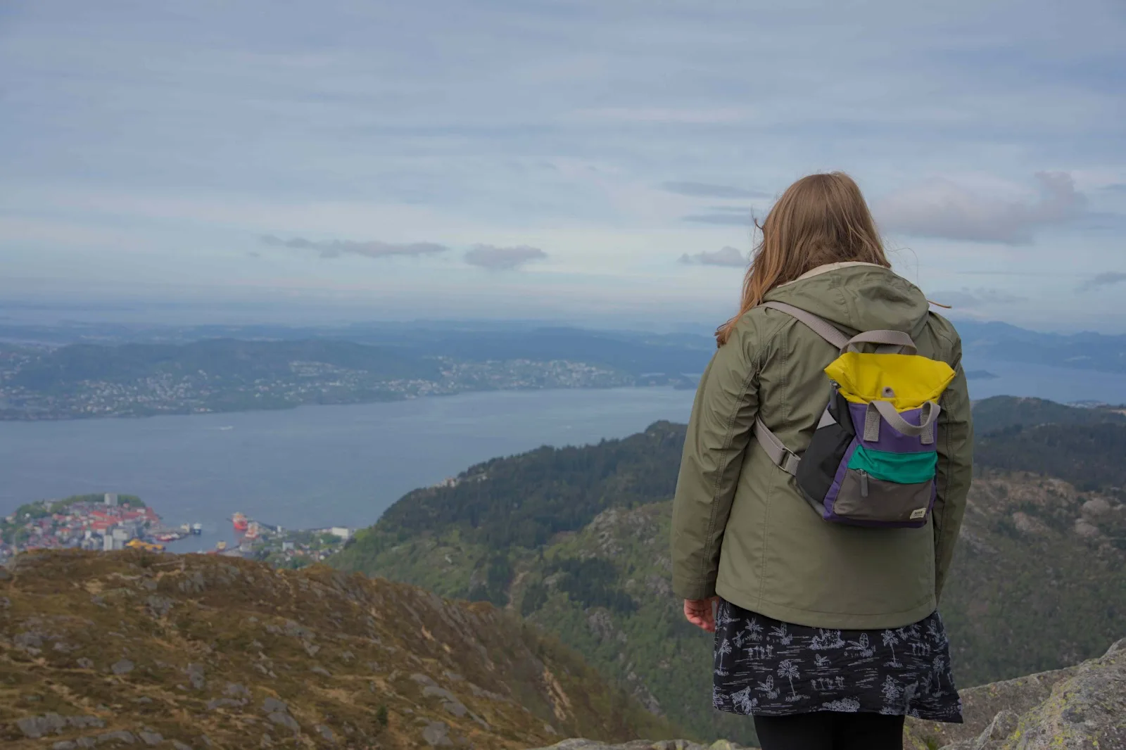 Alice, wearing a colourful backpack, looking out over the water and hills.