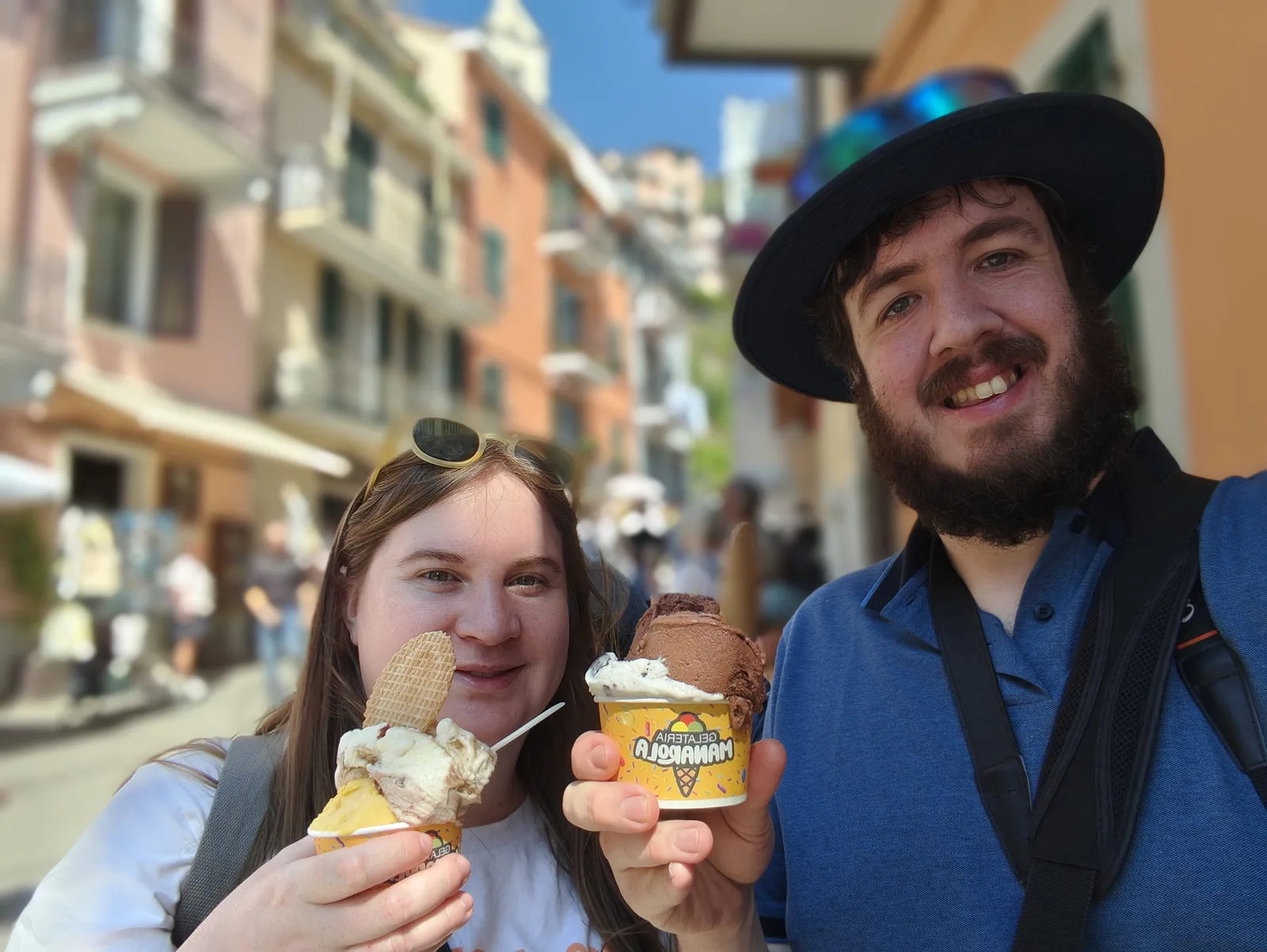 Alice and Robert holding ice creams on a sunny street lined with colourful buildings.
